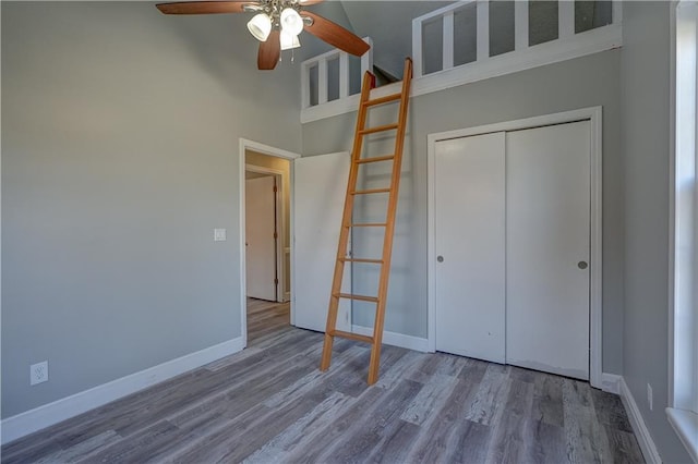 unfurnished bedroom with a ceiling fan, wood finished floors, a closet, a high ceiling, and baseboards