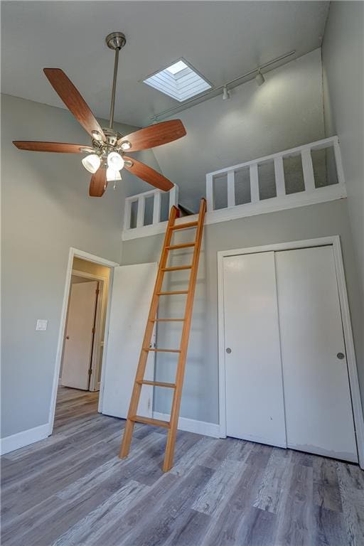 unfurnished bedroom featuring high vaulted ceiling, wood finished floors, a skylight, rail lighting, and baseboards