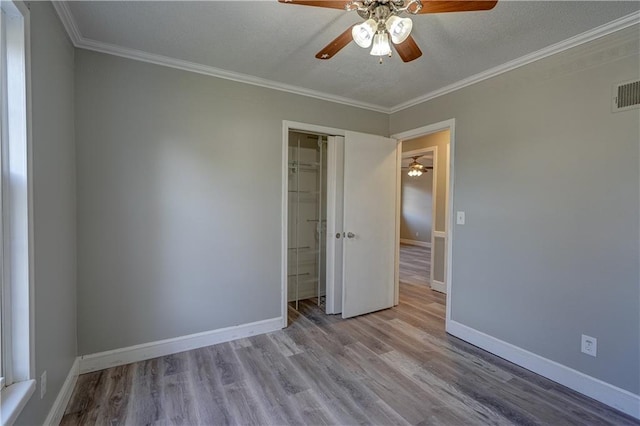 unfurnished bedroom with a textured ceiling, crown molding, baseboards, and wood finished floors