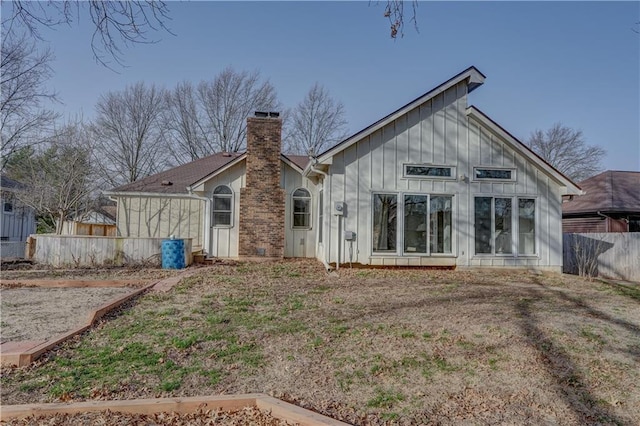 rear view of house featuring fence, board and batten siding, and a chimney