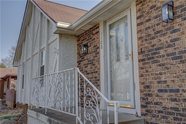 view of exterior entry with brick siding and roof with shingles