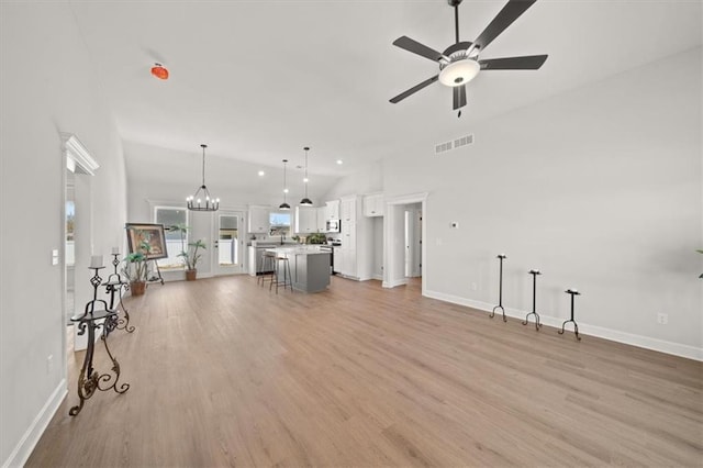 unfurnished living room with light wood finished floors, visible vents, high vaulted ceiling, baseboards, and ceiling fan with notable chandelier