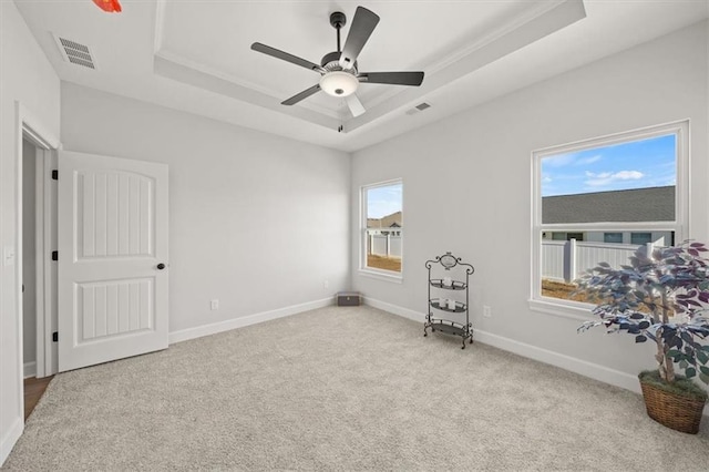 carpeted empty room featuring ceiling fan, a tray ceiling, visible vents, and baseboards