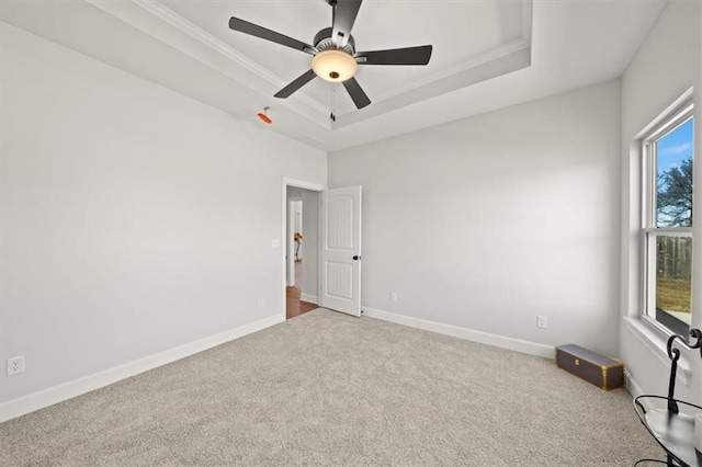 empty room with crown molding, carpet floors, a raised ceiling, and baseboards