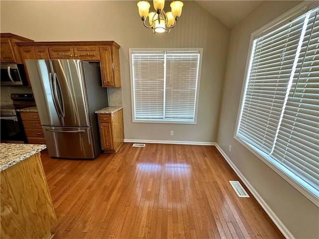 kitchen with lofted ceiling, appliances with stainless steel finishes, brown cabinets, light wood-type flooring, and a notable chandelier