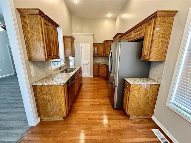 kitchen featuring visible vents, light stone counters, brown cabinets, stainless steel appliances, and a sink