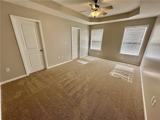 carpeted spare room featuring baseboards, a raised ceiling, and a ceiling fan