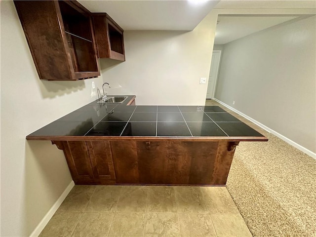 kitchen featuring a peninsula, baseboards, dark brown cabinets, and a sink