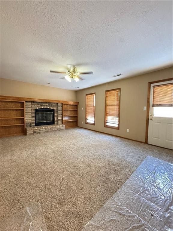 unfurnished living room with visible vents, a fireplace, a wealth of natural light, and carpet