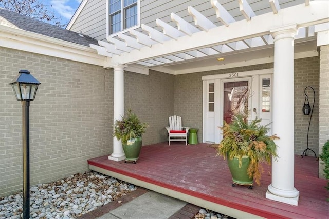 doorway to property featuring brick siding, roof with shingles, and a pergola