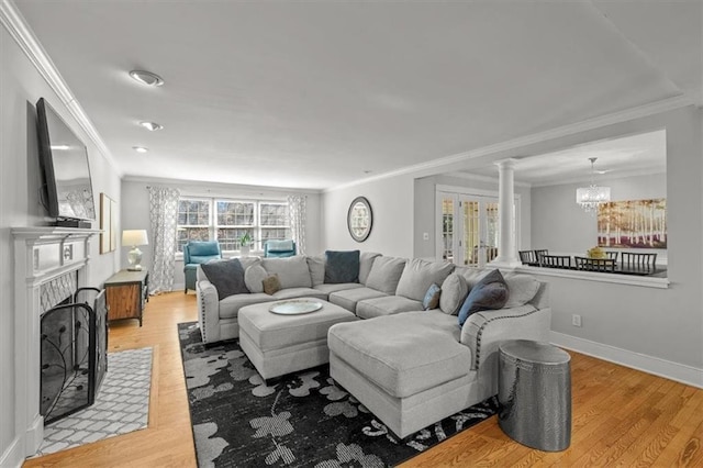 living area with a notable chandelier, ornamental molding, a fireplace with flush hearth, and light wood-style floors