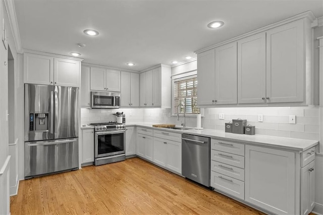 kitchen with stainless steel appliances, light wood finished floors, a sink, and light countertops