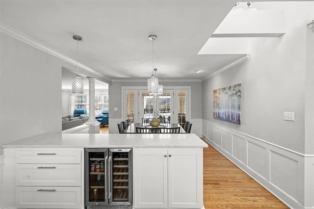 bar with light wood-type flooring, wine cooler, ornamental molding, and wainscoting