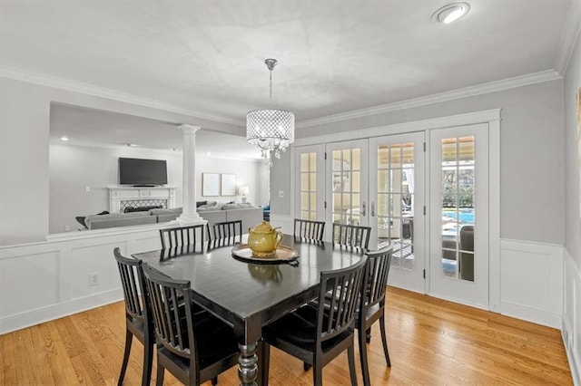 dining area with light wood-style flooring, a fireplace, crown molding, and wainscoting