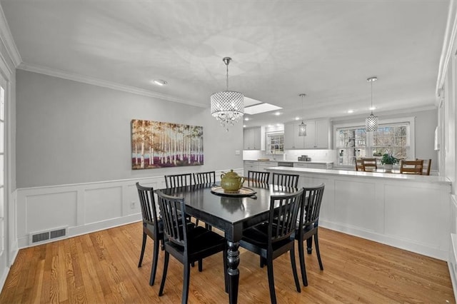 dining area with ornamental molding, light wood-type flooring, a chandelier, and visible vents