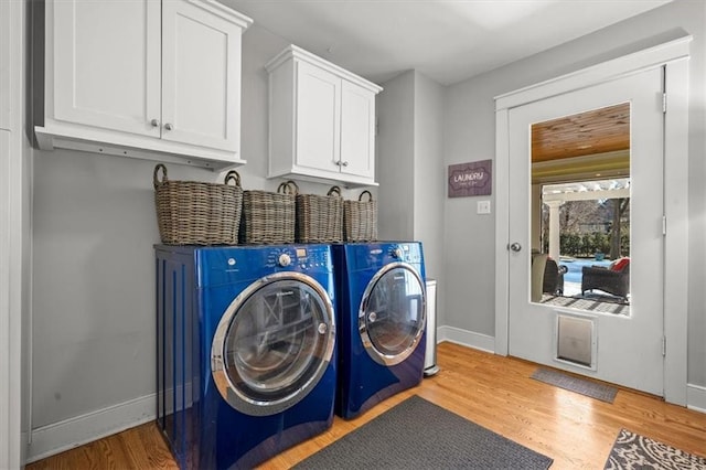 clothes washing area with light wood-type flooring, washing machine and dryer, cabinet space, and baseboards