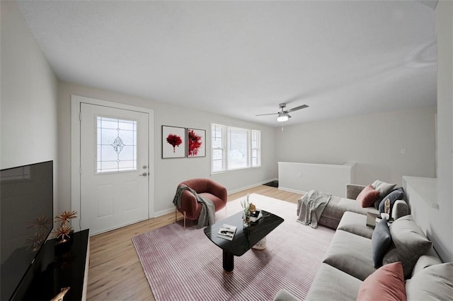 living area featuring a ceiling fan, baseboards, and light wood finished floors