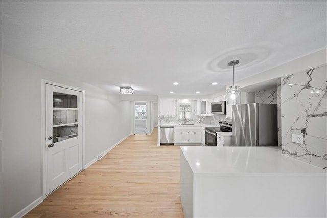 kitchen featuring stainless steel appliances, light countertops, light wood-style flooring, white cabinetry, and a peninsula