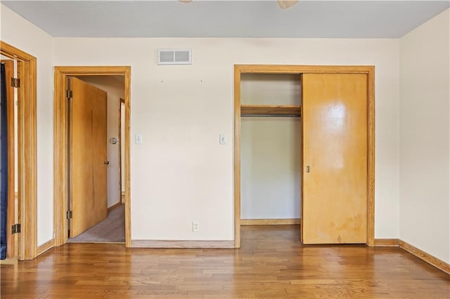 unfurnished bedroom featuring baseboards, a closet, visible vents, and wood finished floors