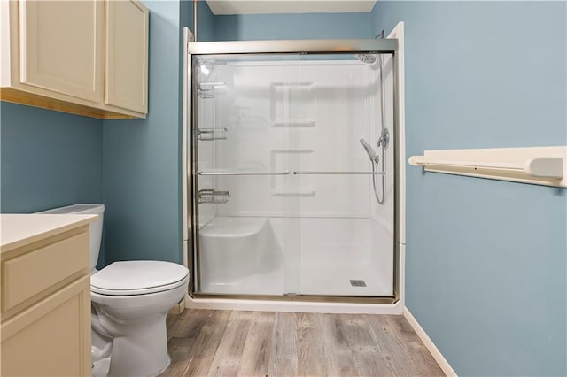 bathroom with toilet, a shower stall, vanity, wood finished floors, and baseboards