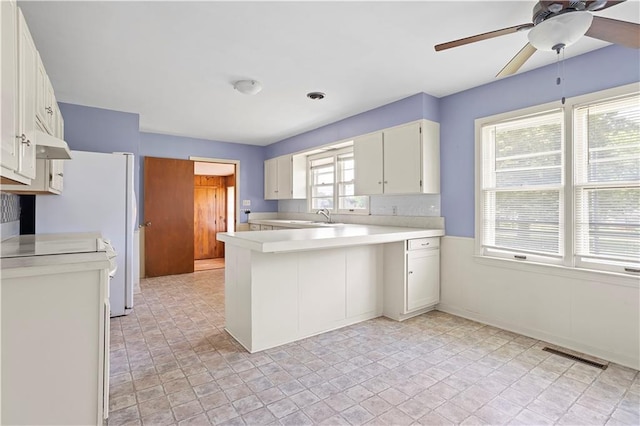 kitchen with under cabinet range hood, a peninsula, visible vents, white cabinets, and light countertops