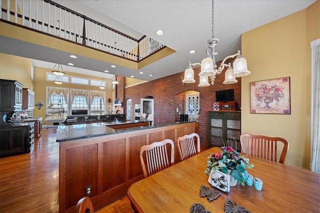 dining space with wood finished floors, brick wall, an inviting chandelier, recessed lighting, and a towering ceiling