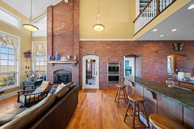 living area with a brick fireplace, light wood-style flooring, arched walkways, and high vaulted ceiling