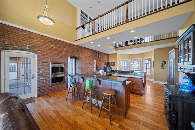 kitchen with a breakfast bar area, light wood finished floors, a spacious island, a high ceiling, and double oven