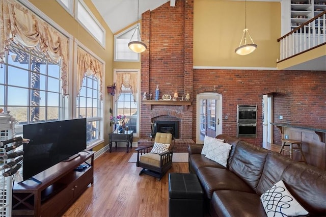 living area featuring wood finished floors, baseboards, brick wall, high vaulted ceiling, and a fireplace