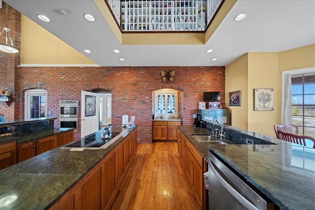 kitchen featuring dark stone counters, a sink, light wood-style floors, appliances with stainless steel finishes, and brown cabinets