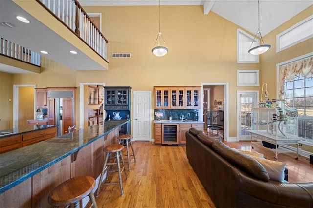 living room featuring light wood finished floors, visible vents, indoor bar, wine cooler, and beamed ceiling