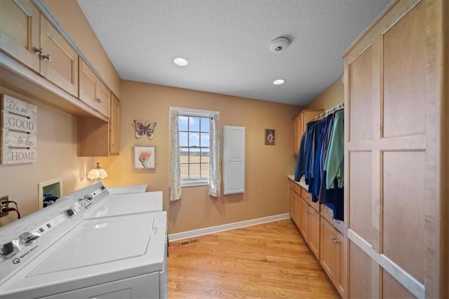 laundry room featuring a textured ceiling, cabinet space, light wood-style floors, baseboards, and washing machine and clothes dryer