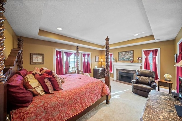 carpeted bedroom featuring a fireplace with flush hearth, recessed lighting, a textured ceiling, and a raised ceiling