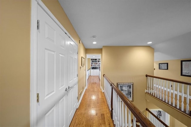 hallway with light wood finished floors, baseboards, lofted ceiling, an upstairs landing, and recessed lighting