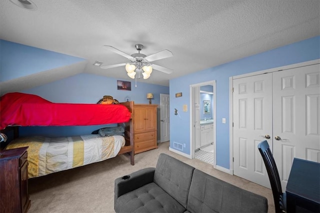 carpeted bedroom with ensuite bath, vaulted ceiling, a closet, a textured ceiling, and a ceiling fan