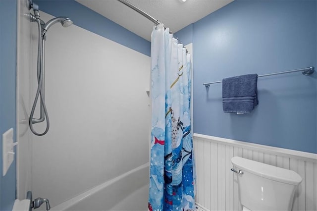 full bath with a textured ceiling, toilet, shower / bathtub combination with curtain, and wainscoting