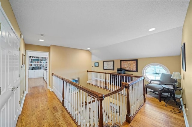 corridor with a textured ceiling, recessed lighting, light wood-style floors, baseboards, and vaulted ceiling