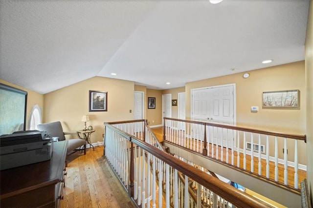 corridor with baseboards, lofted ceiling, an upstairs landing, recessed lighting, and wood finished floors