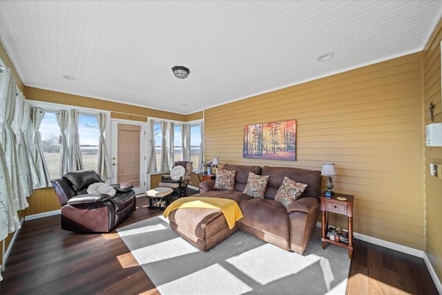 living area featuring wooden walls, wood finished floors, baseboards, and a sunroom