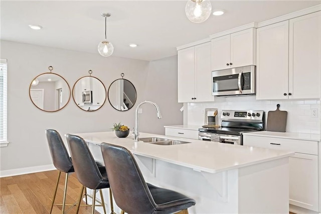 kitchen featuring white cabinets, a kitchen island with sink, stainless steel appliances, light countertops, and a sink