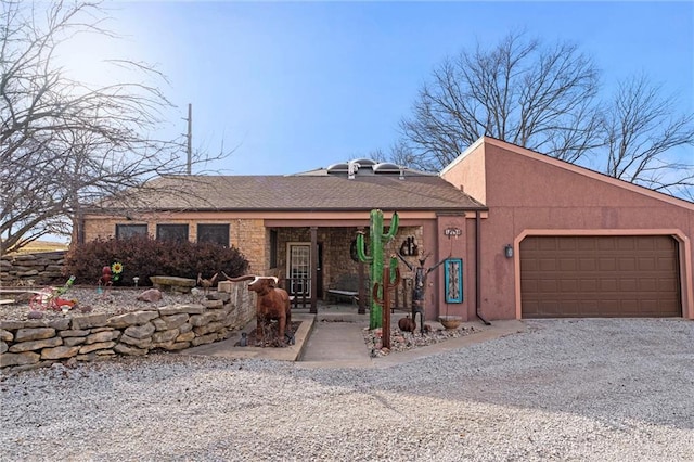 view of front of home with an attached garage, gravel driveway, and stucco siding