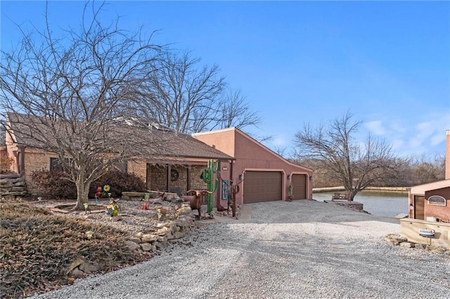 view of front facade with gravel driveway, a water view, an attached garage, and stucco siding