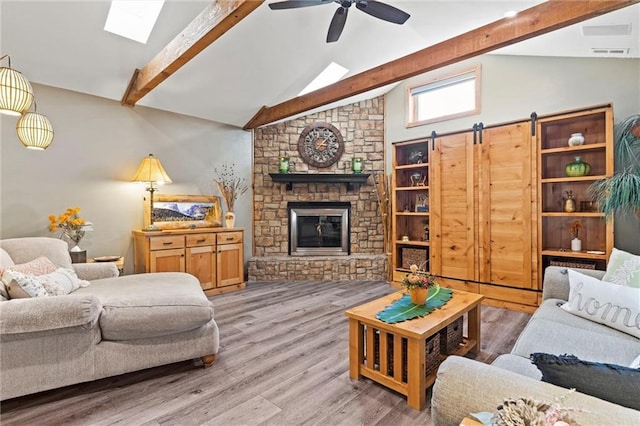 living room with beam ceiling, visible vents, ceiling fan, a stone fireplace, and wood finished floors