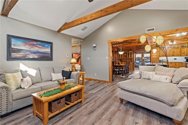 living room featuring baseboards, visible vents, light wood-type flooring, high vaulted ceiling, and beam ceiling