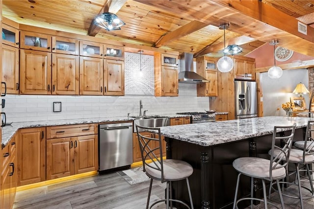 kitchen featuring decorative backsplash, wall chimney exhaust hood, appliances with stainless steel finishes, a kitchen breakfast bar, and light wood-type flooring