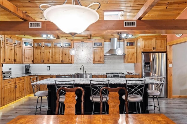 kitchen featuring wall chimney exhaust hood, visible vents, a sink, and stainless steel fridge with ice dispenser