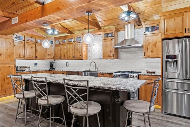 kitchen featuring a center island, light wood-style flooring, decorative backsplash, appliances with stainless steel finishes, and wall chimney exhaust hood