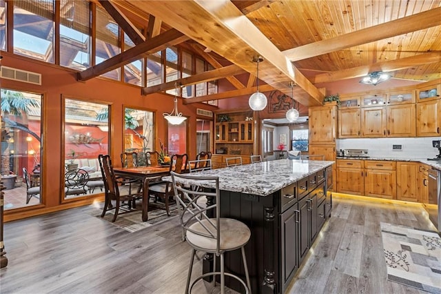 kitchen featuring pendant lighting, light wood finished floors, visible vents, backsplash, and light stone countertops