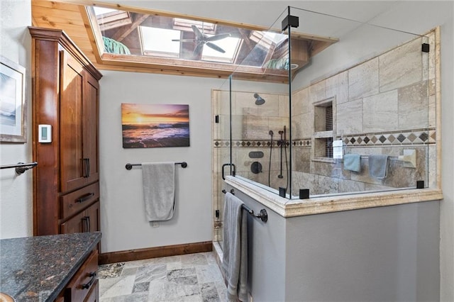 bathroom featuring tiled shower, vanity, stone tile flooring, and baseboards