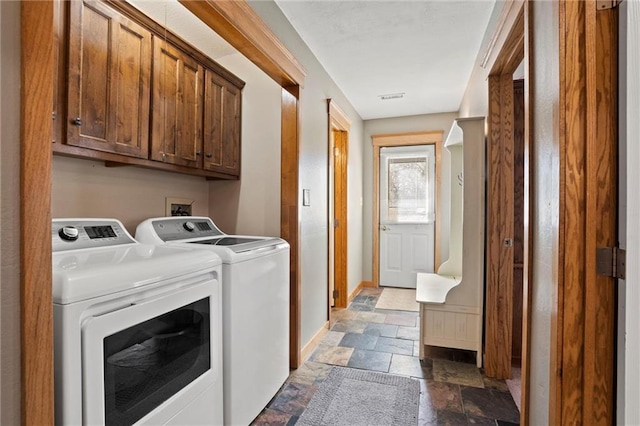 clothes washing area with washing machine and clothes dryer, stone tile floors, cabinet space, visible vents, and baseboards